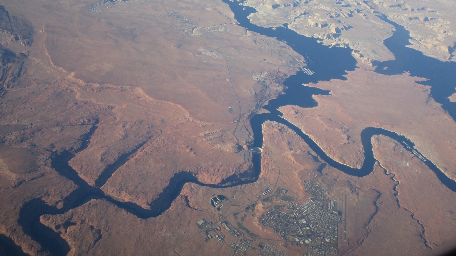 Aerial photo of Lake Powell winding through red desert rock, with Glen Canyon Dam, Wahweap Marina, and the town of Page, Arizona all visible