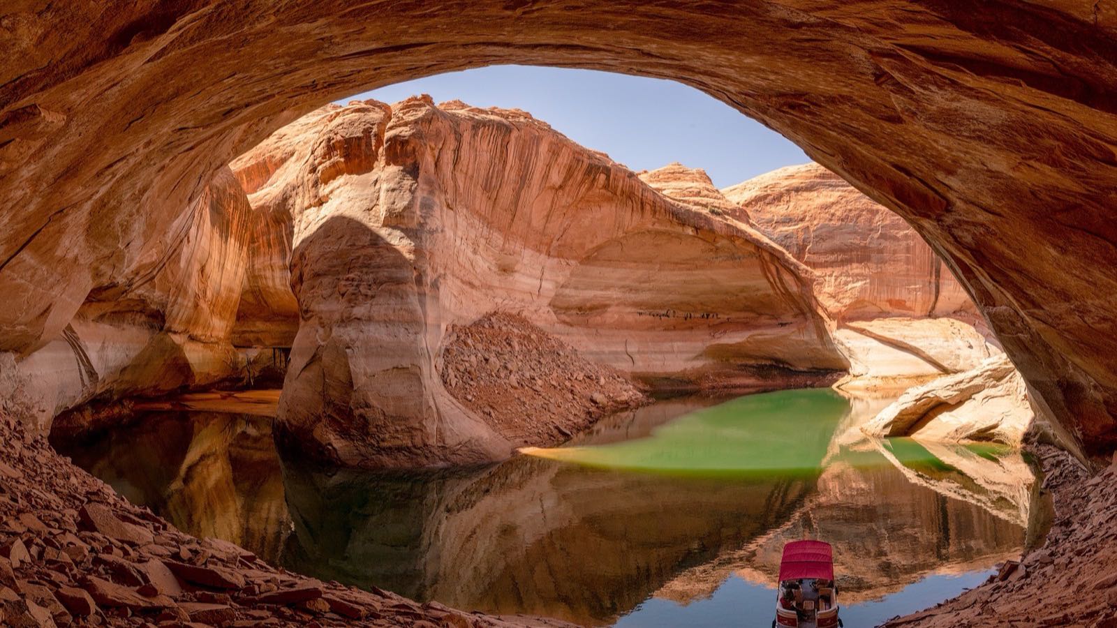 Cathedral in the Desert at low water — a small boat floats on green water inside the huge sandstone alcove re-exposed by Lake Powell's decline